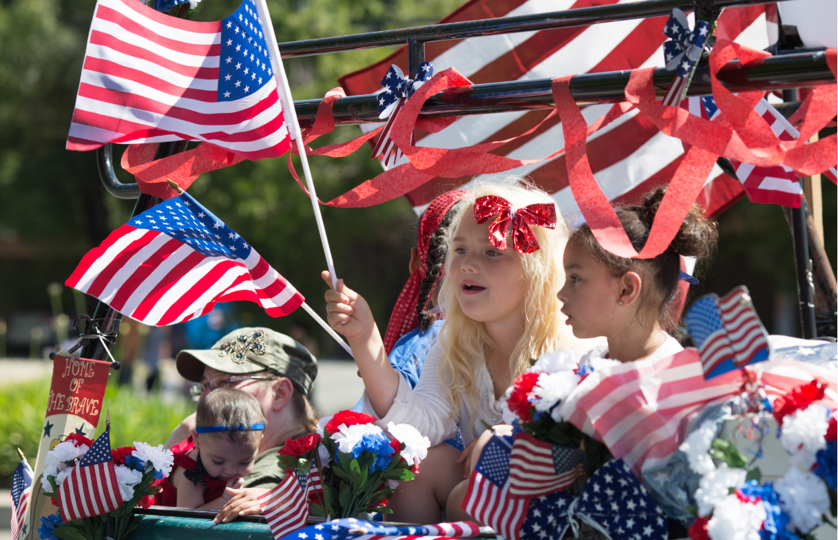 Children ride a decorated parade float with American flags and red, white, and blue streamers during a patriotic celebration.