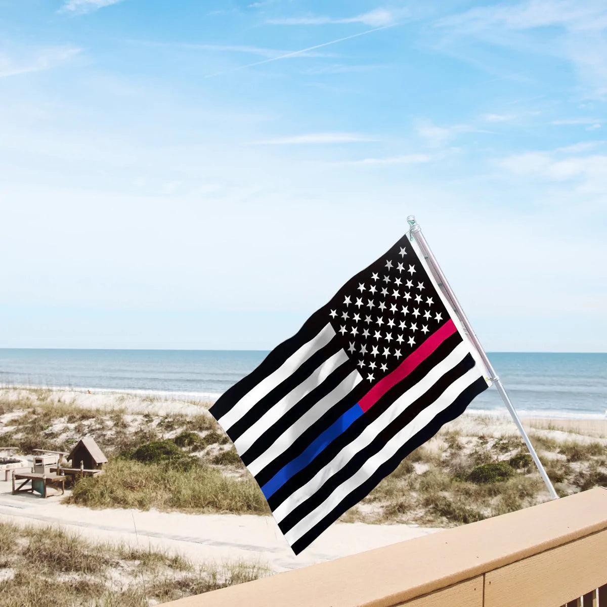 A 3×5 Ft Embroidery Thin Blue Line Thin Red Line Flag Made in USA by Jetlifee, featuring a black and white American flag with red and blue stripes to support first responders, waves on a beach with sand dunes and the ocean in the background. This heavyweight nylon police enforcement flag is durable and strong, standing resilient against the coastal winds.